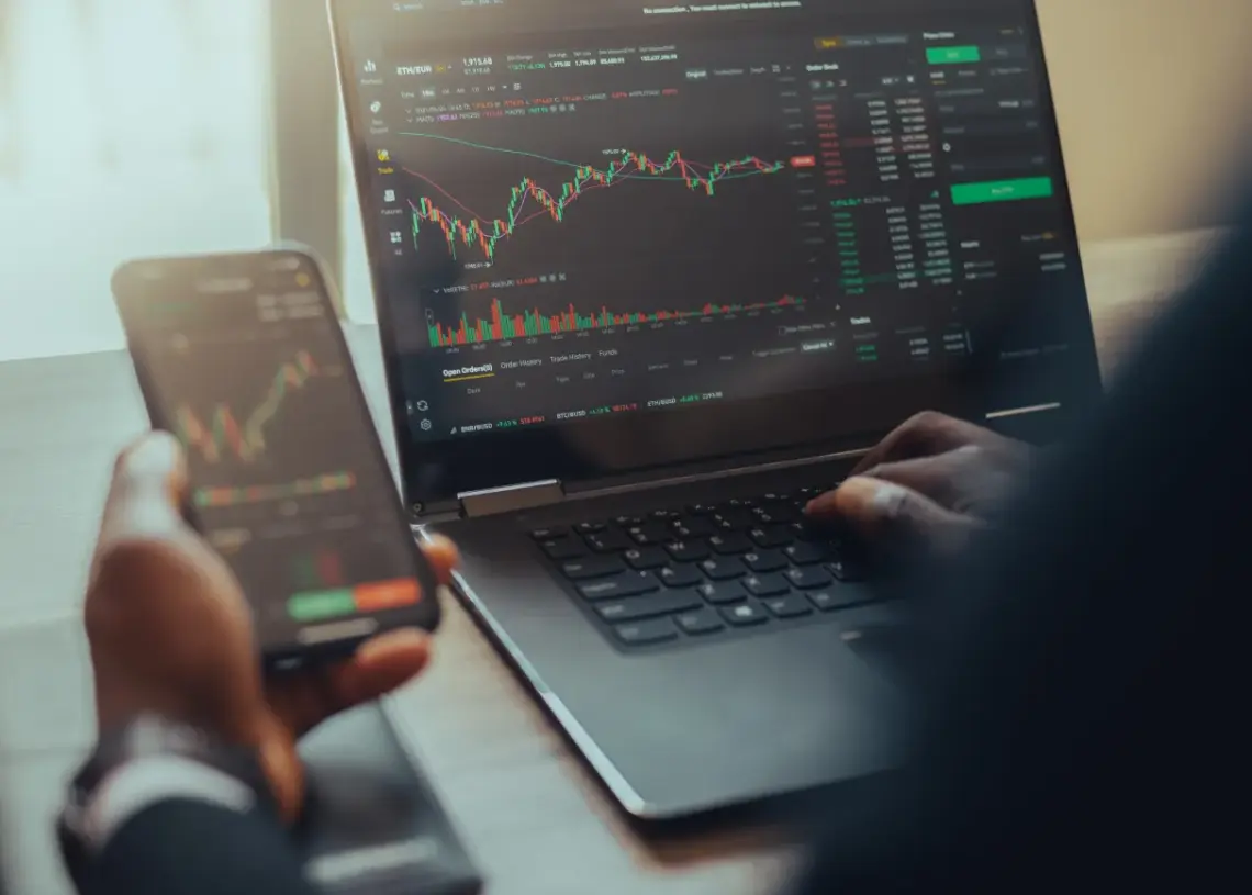 person using laptop and phone for stock analysis