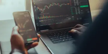 person using laptop and phone for stock analysis
