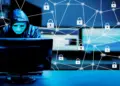 hooded hacker working on computer in dark