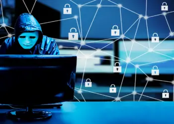 hooded hacker working on computer in dark
