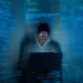 hooded young adult using laptop in dark room
